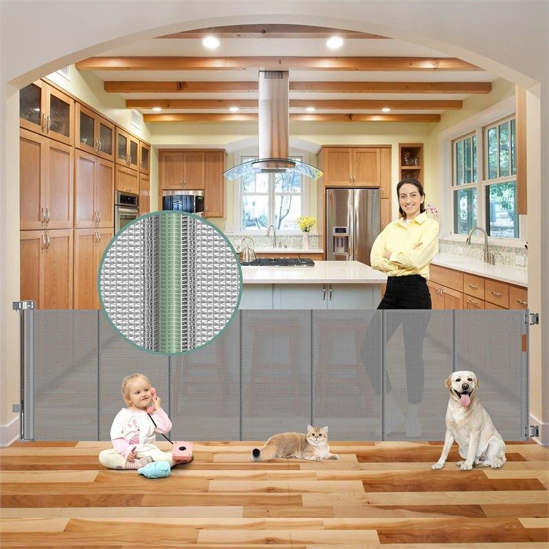 Gray retractable mesh safety gate spanning wide kitchen opening with toddler, cat, and golden retriever in lifestyle photo